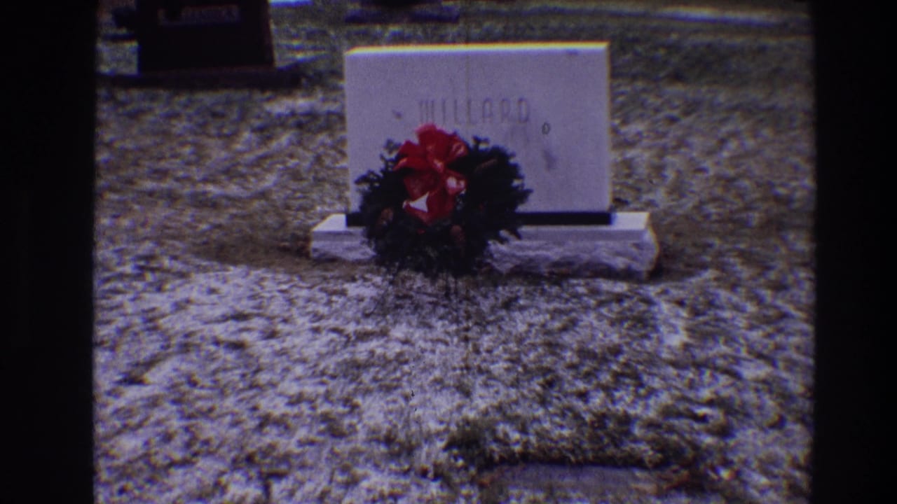MILLARD grave marker with wreath and red bow in cemetery grass.