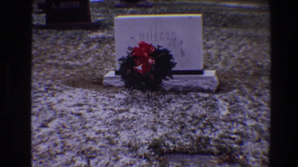 The MILLARD headstone remains centered, with a wreath and red bow visible against muted cemetery grass in the 1968 Toledo footage.