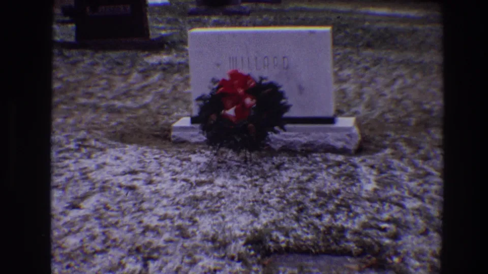 A closer handheld 8mm view shows the white MILLARD headstone and wreath with red bow in a Toledo cemetery setting.