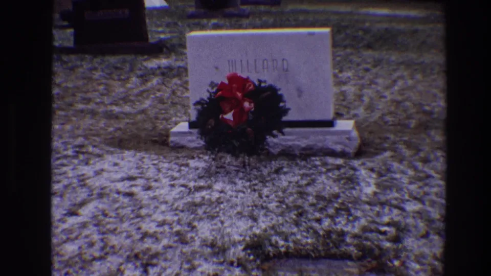 1968 Toledo home-movie still of the Willard grave marker with a red-bowed wreath against wintery grass.