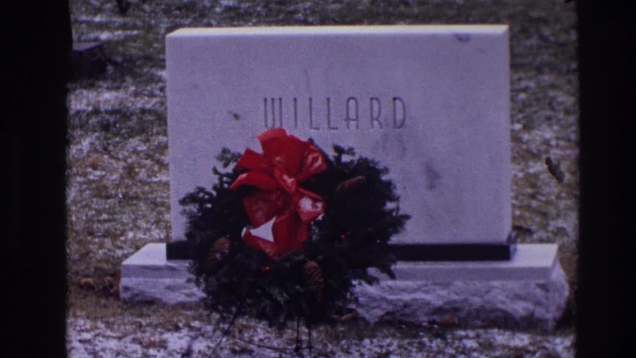 White WILLARD gravestone with wreath, red bow, pinecones, winter grass, and snow patches.