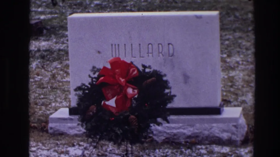 1968 Toledo 8mm frame showing a gray WILLARD grave marker with a red-bowed Christmas wreath on snowy cemetery ground.