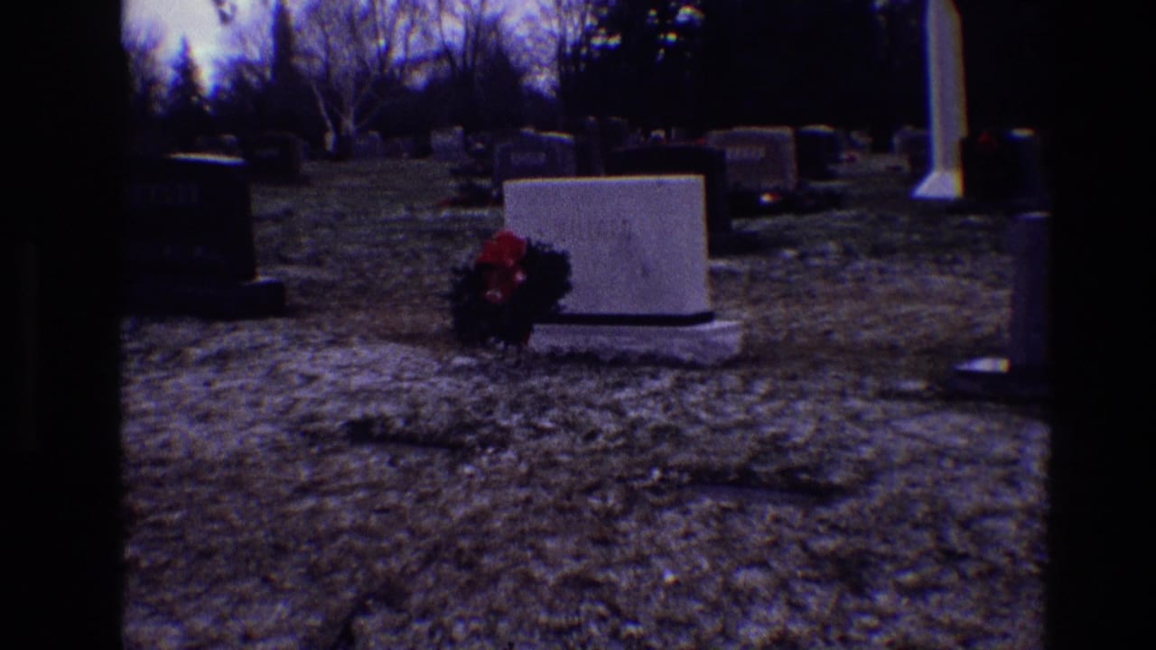 Cemetery grounds with a low white headstone and red wreath in front.