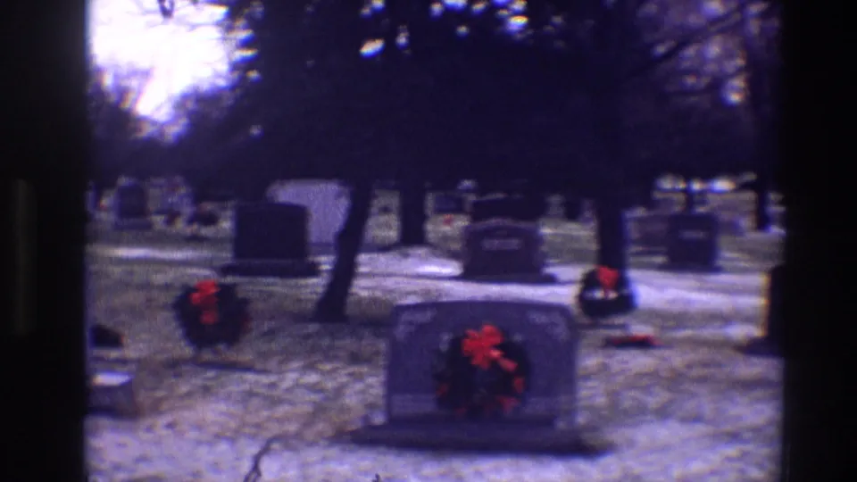 1968 Toledo cemetery view with wreath-marked tombstones, snow-dusted ground, bare trees, and dark 8mm frame edges.