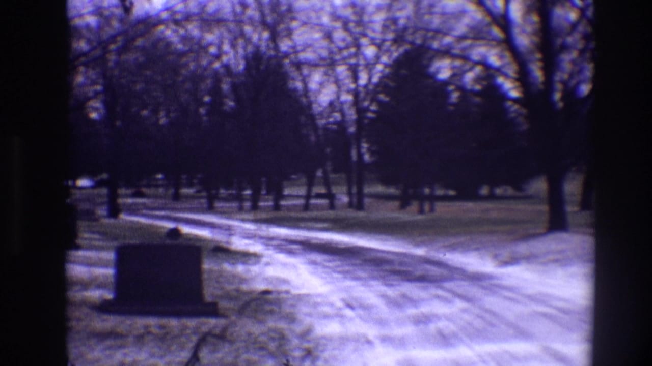 Curving icy cemetery road with headstones, bare trees, and winter grass.