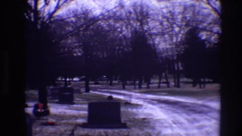 1968 Toledo cemetery view with a curving snowy path, grey tombstones, bare trees, and a red wreath near the foreground.