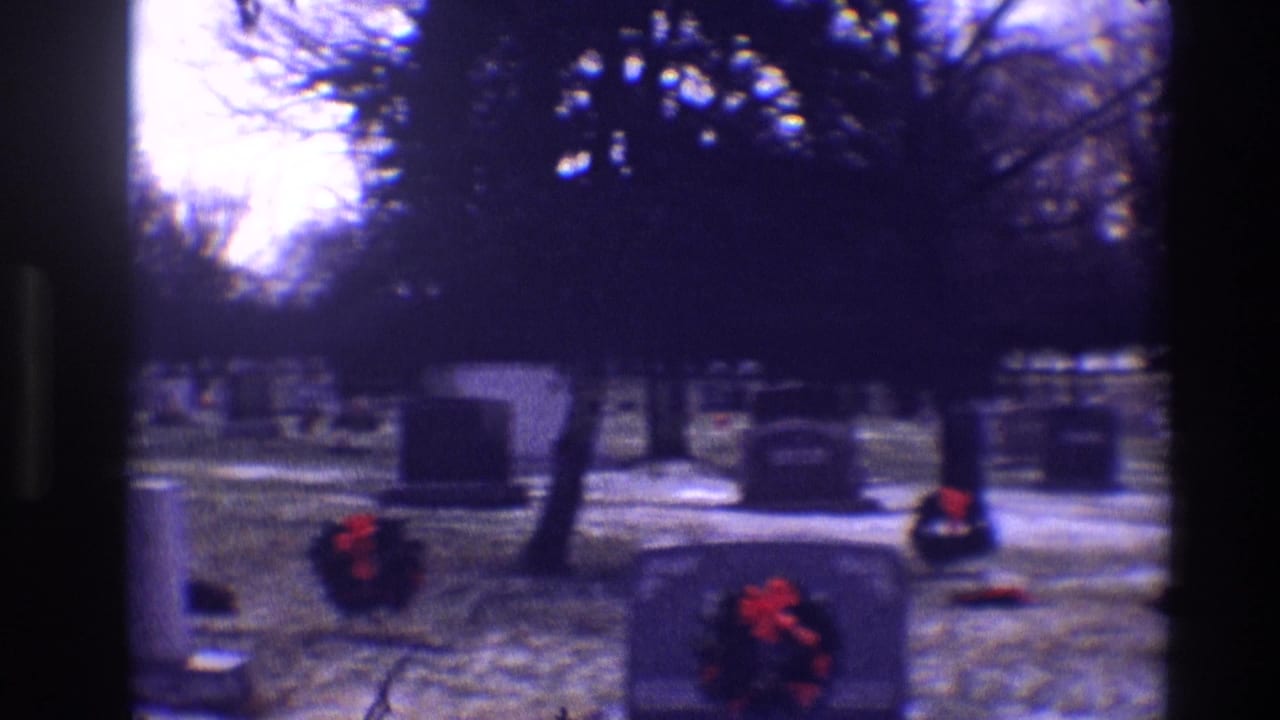 Grey cemetery headstones with red wreaths on snow-dusted grass.
