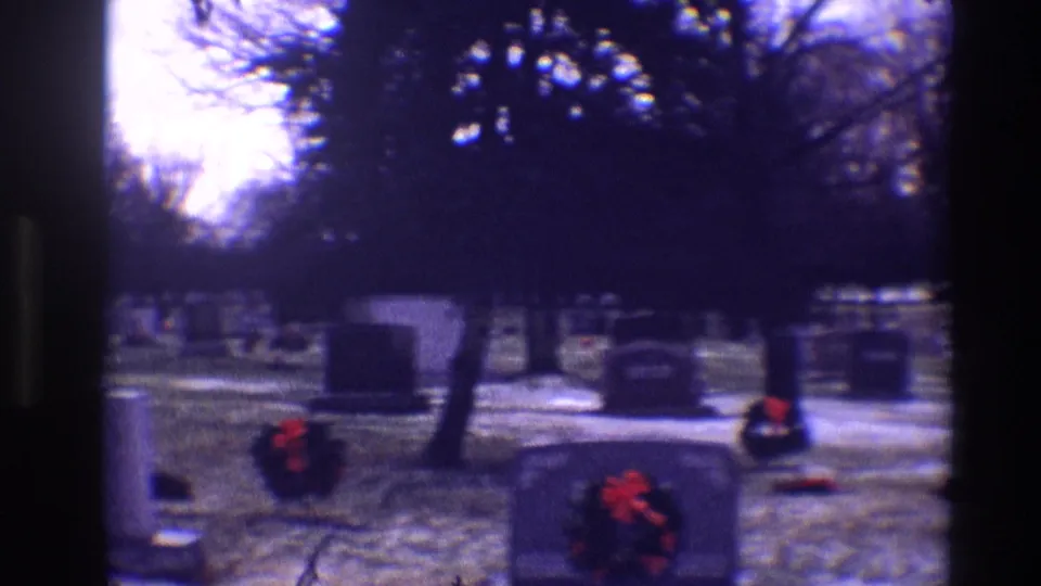 1968 Toledo cemetery grounds showing several grey tombstones, red Christmas wreaths, bare trees, and light snow under a cloudy sky.