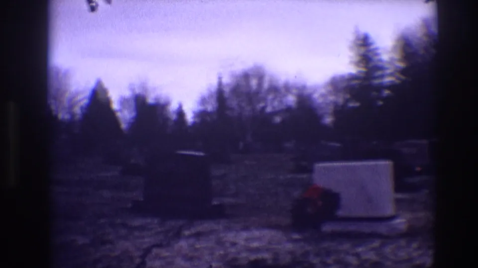 1968 Toledo cemetery scene with darkened exposure, grey grave markers, red wreaths, bare trees, and snow on the grass.