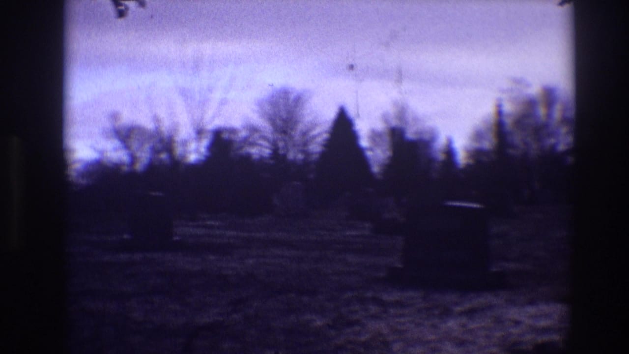 Dark cemetery grounds with grave markers, bare trees, and a purple dusk sky.