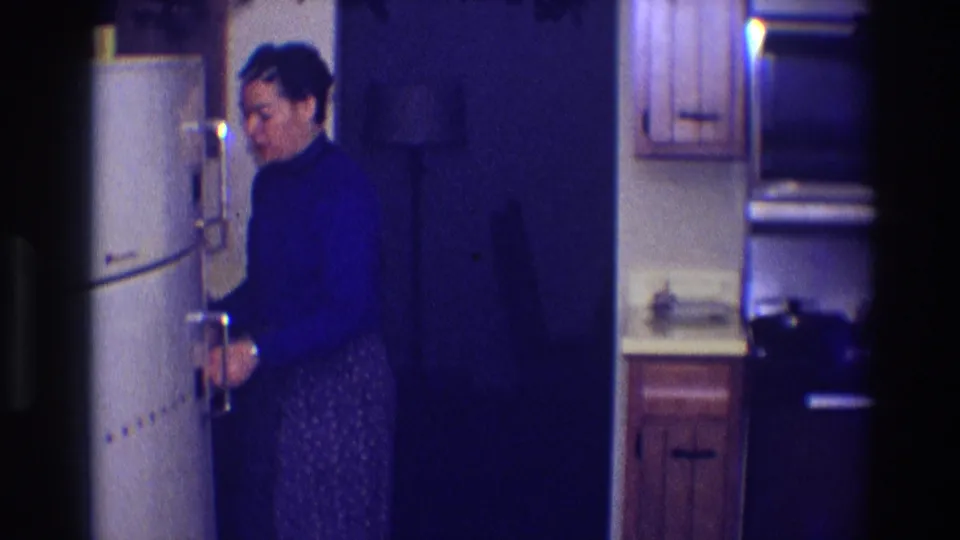 Woman in a dark turtleneck stands beside a rounded refrigerator in a dim Toledo kitchen, 1968.
