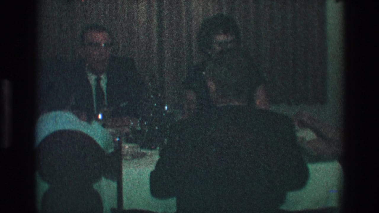 Adults at a dimly lit Toledo dinner party in 1968, seated around a table with glassware and dark drapery behind them.