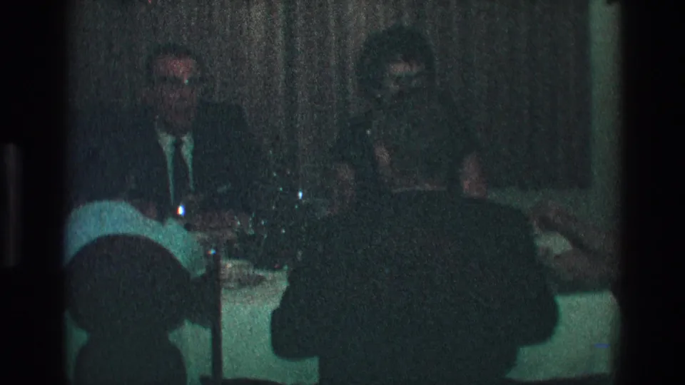 Adults at a dimly lit Toledo dinner party in 1968, seated around a table with glassware and dark drapery behind them.