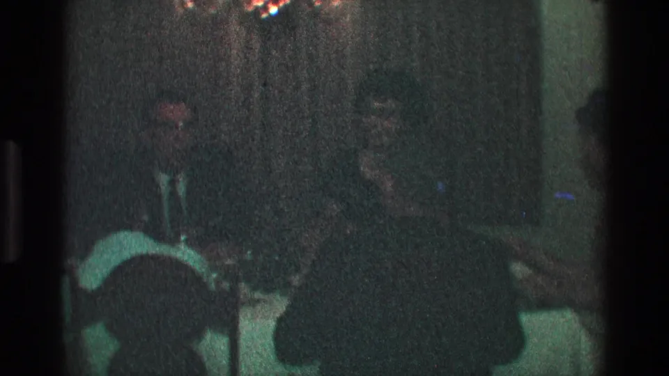 1968 Toledo home-movie still of formally dressed adults gathered at a dimly lit dinner table.