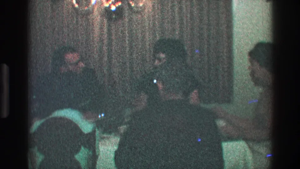 1968 Toledo home-movie frame of adults seated around a formal dining table in a private interior.