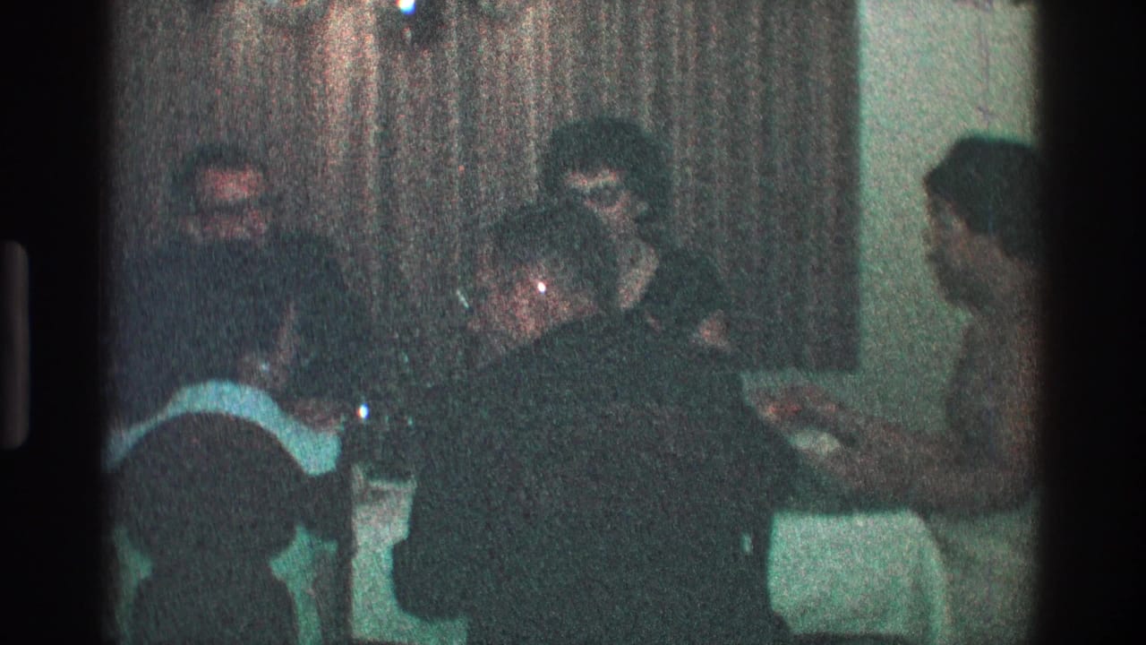 Person in the foreground leans over a dinner table while others sit behind.