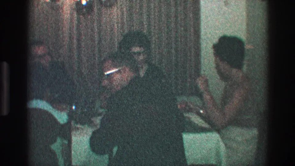 In the Toledo home interior, adults sit around the dinner table as one person with glasses turns toward the group.
