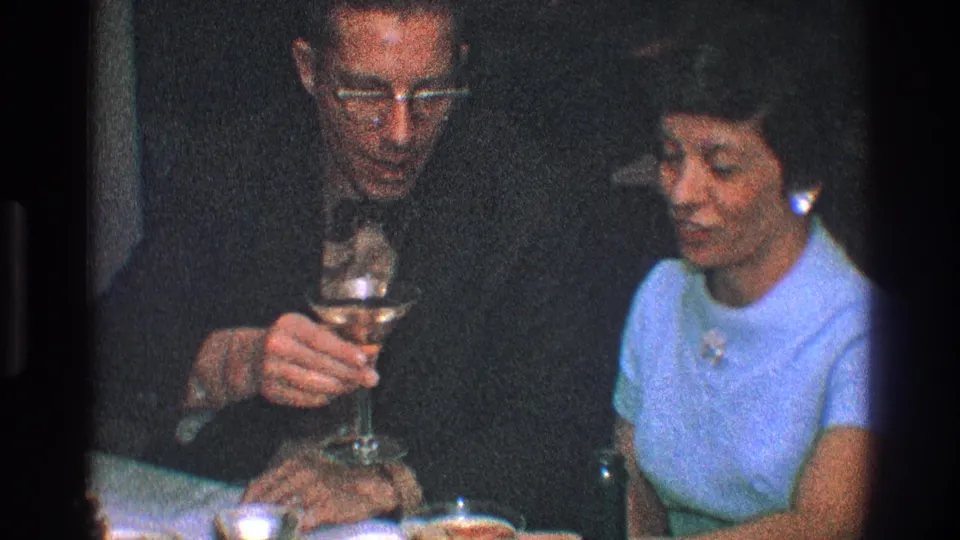 1968 Toledo frame of a seated man and woman in conversation as the man holds a cocktail glass near the table.