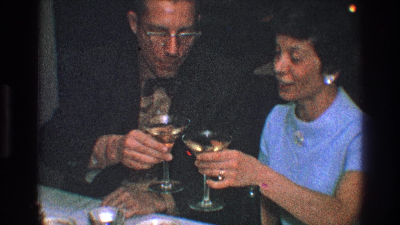 Man and woman clink martini glasses at a dim dinner table.