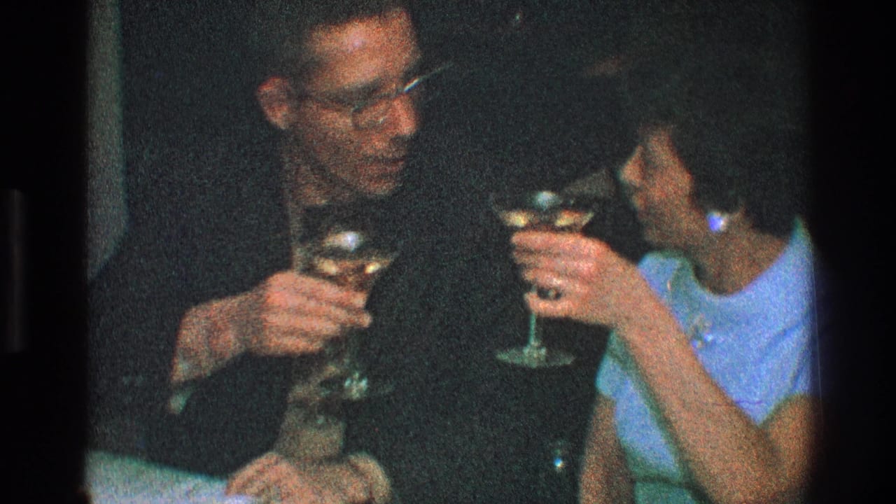Man and woman hold raised martini glasses while seated close together.