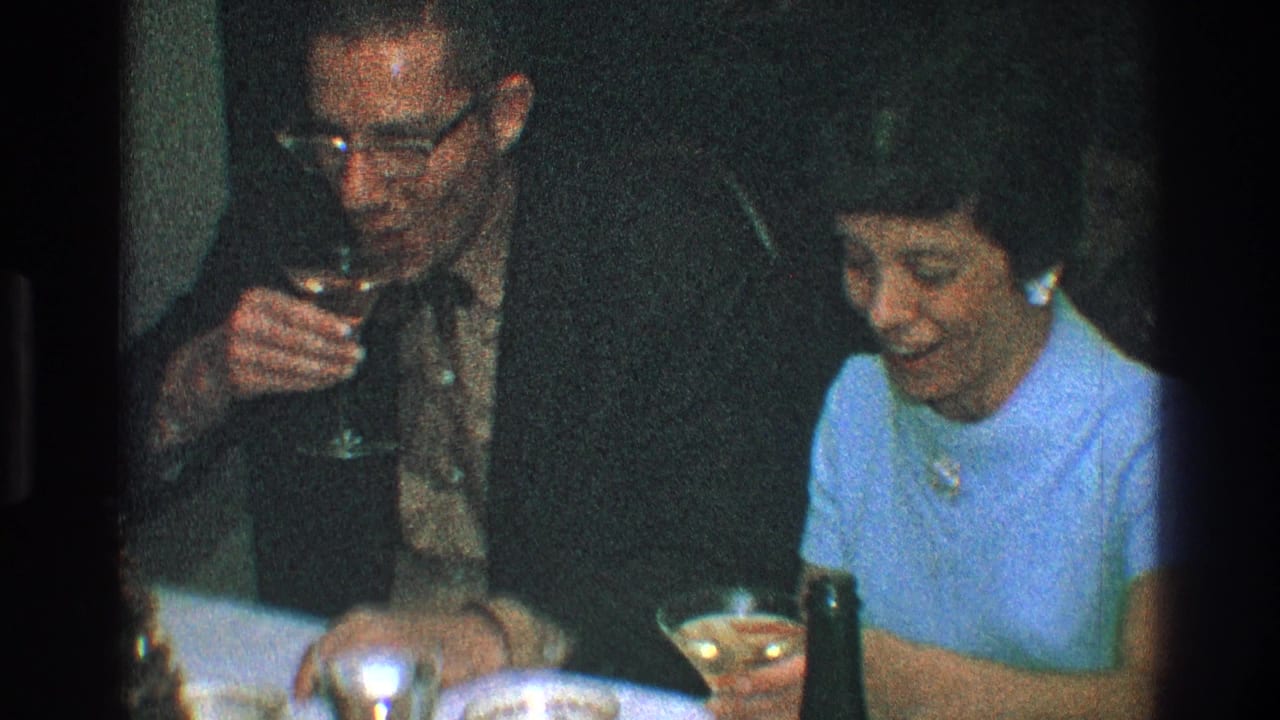 Man and woman hold drinks while seated together at a dinner table.