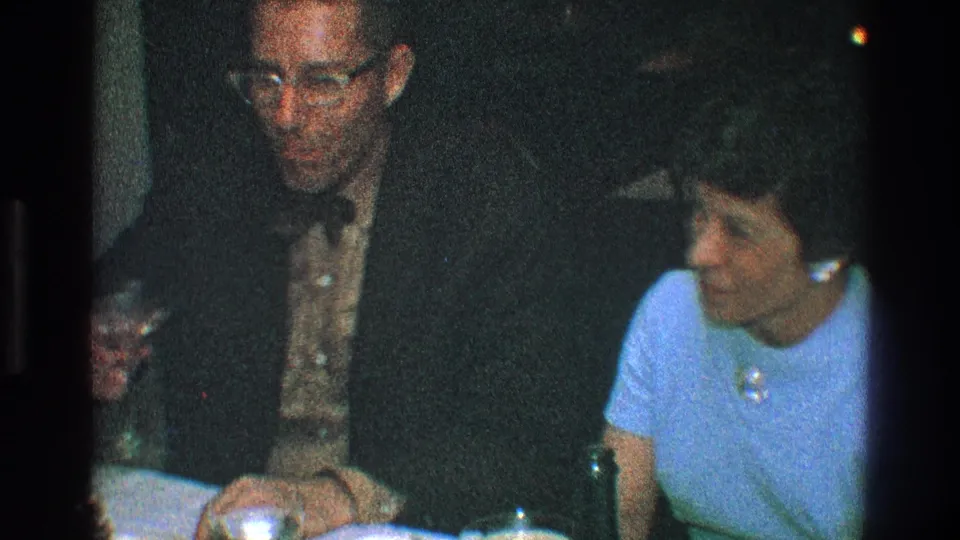 A man in a dark suit and a woman in a light blue dress sit side by side with drinks on the table in Toledo, Ohio, 1968.