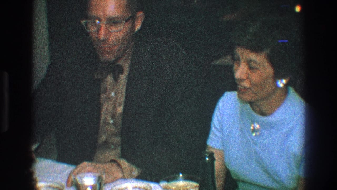 Man in a dark suit sits beside a woman in a light blue dress at a table.
