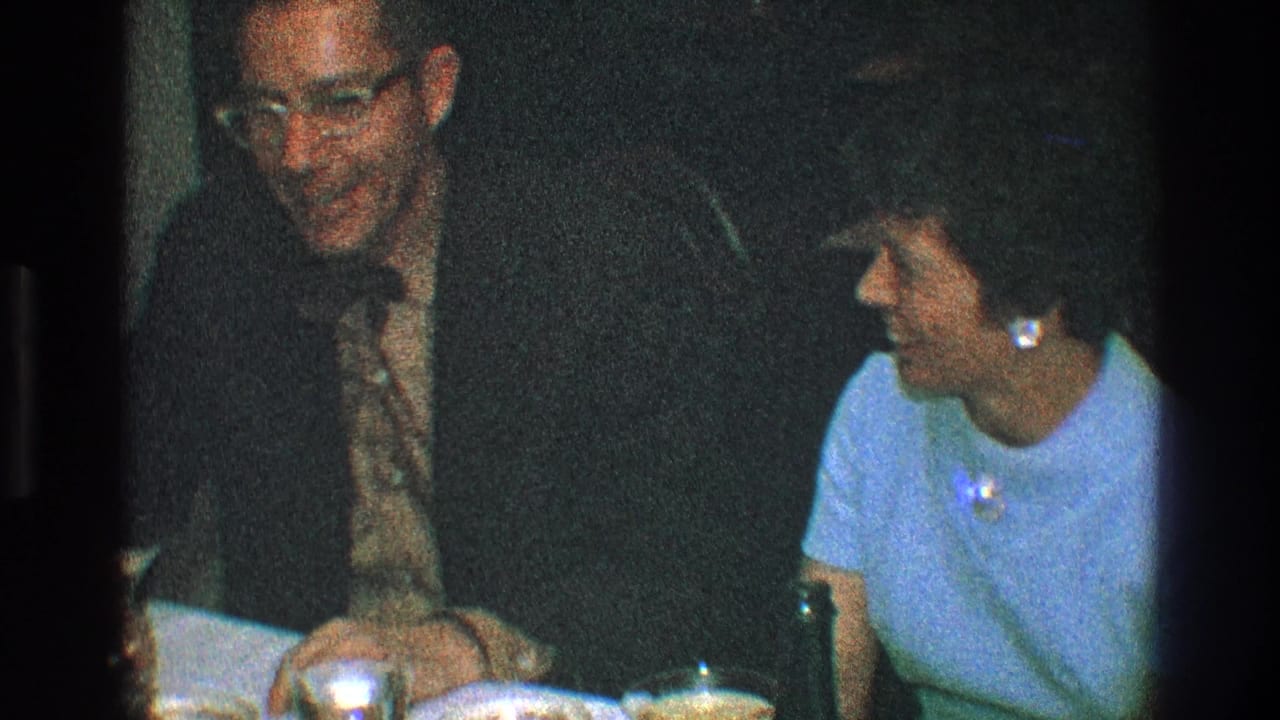 Man in glasses smiles toward a woman seated beside him at dinner.