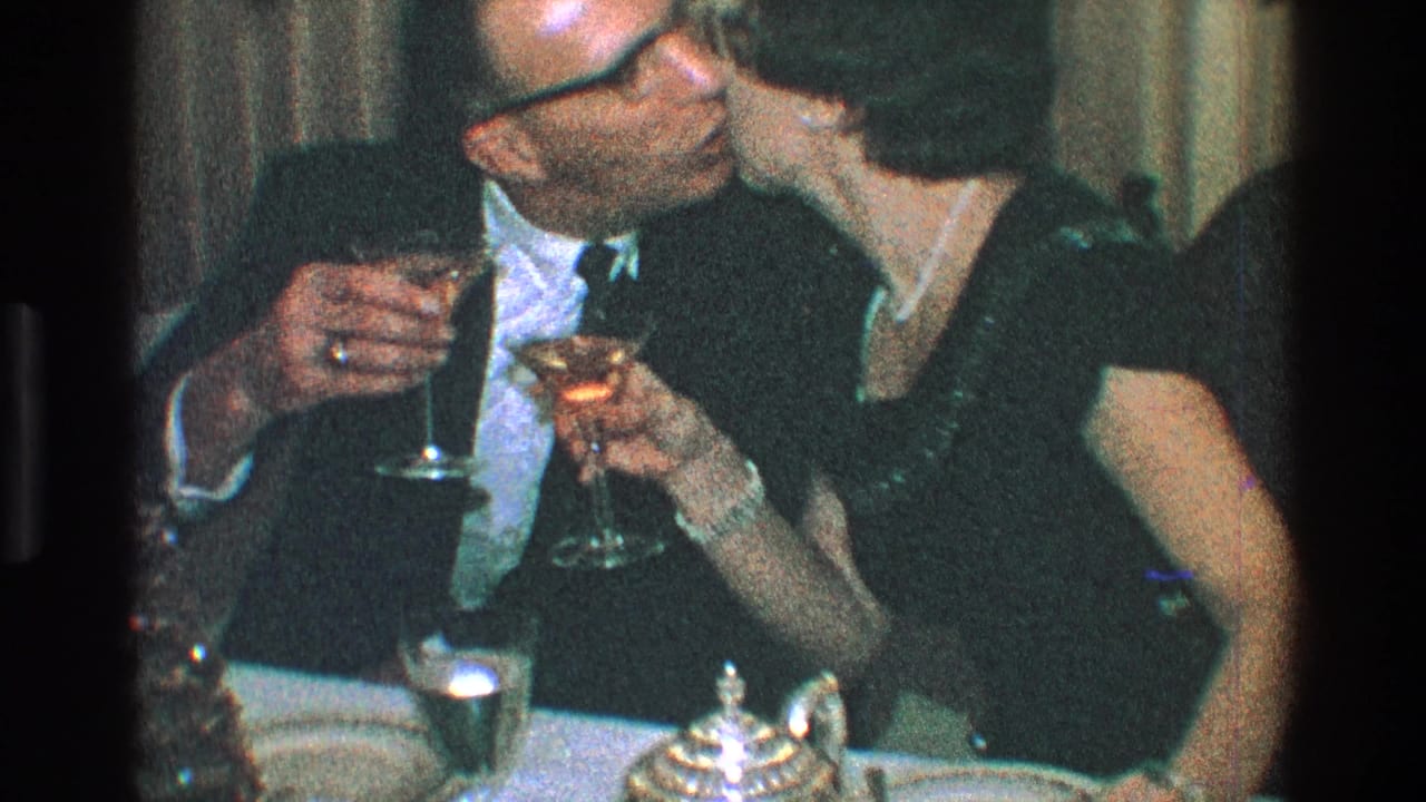 Couple leans in and kisses while holding cocktail glasses.