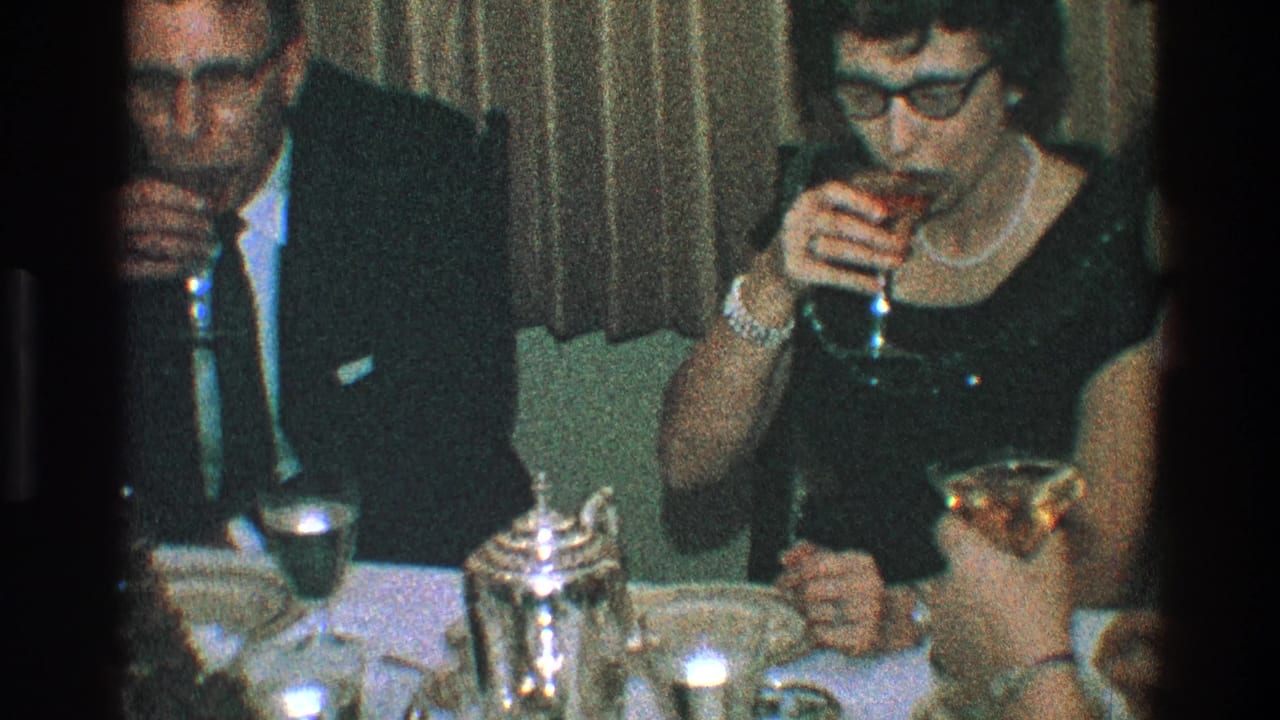 1968 Toledo home-movie frame of adults in formal clothing seated at a table with glasses, plates, and silver table service.