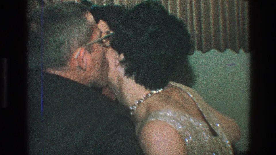 A woman in a sequined dress and glasses gives a cheek kiss to a man during the 1968 Toledo dinner gathering.