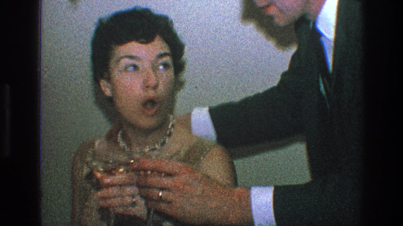 Woman holding a glass looks toward a suited man leaning in beside her.