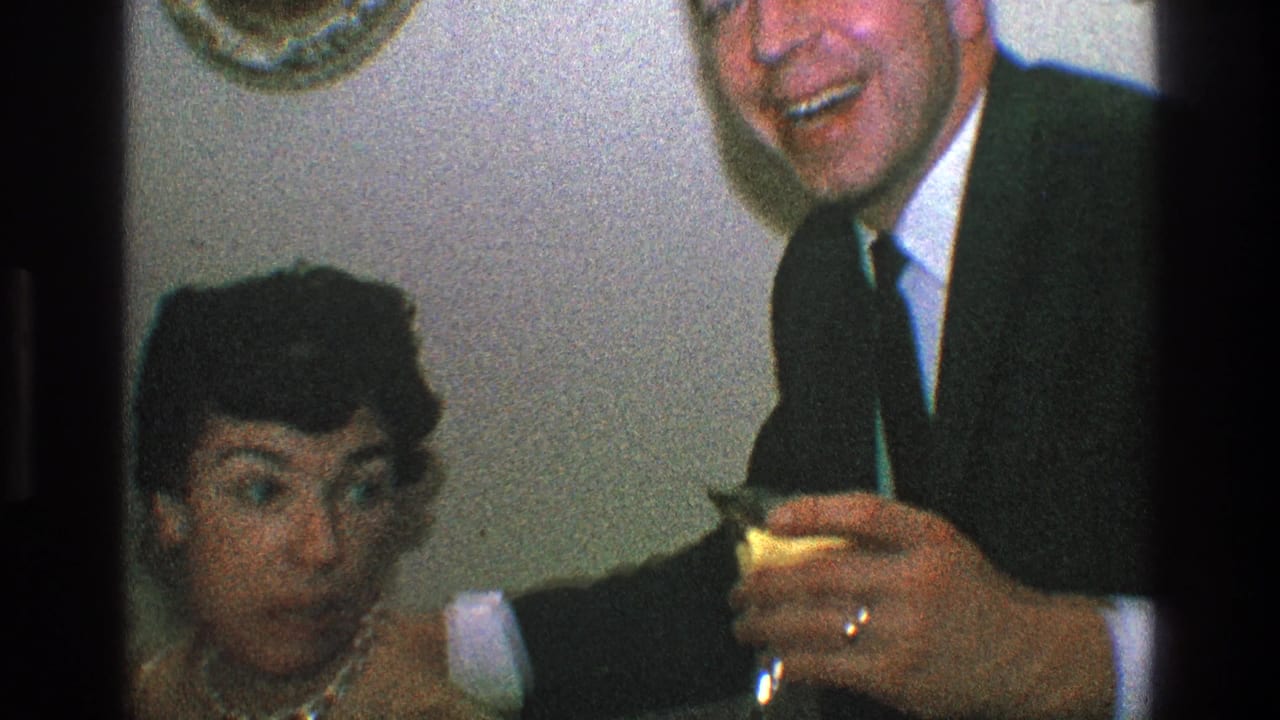 Woman and suited man laughing at an indoor party while holding drinks.
