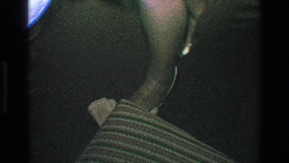 A dim handheld party frame shows dark clothing, a striped fabric surface, and a pale object near the lower center.