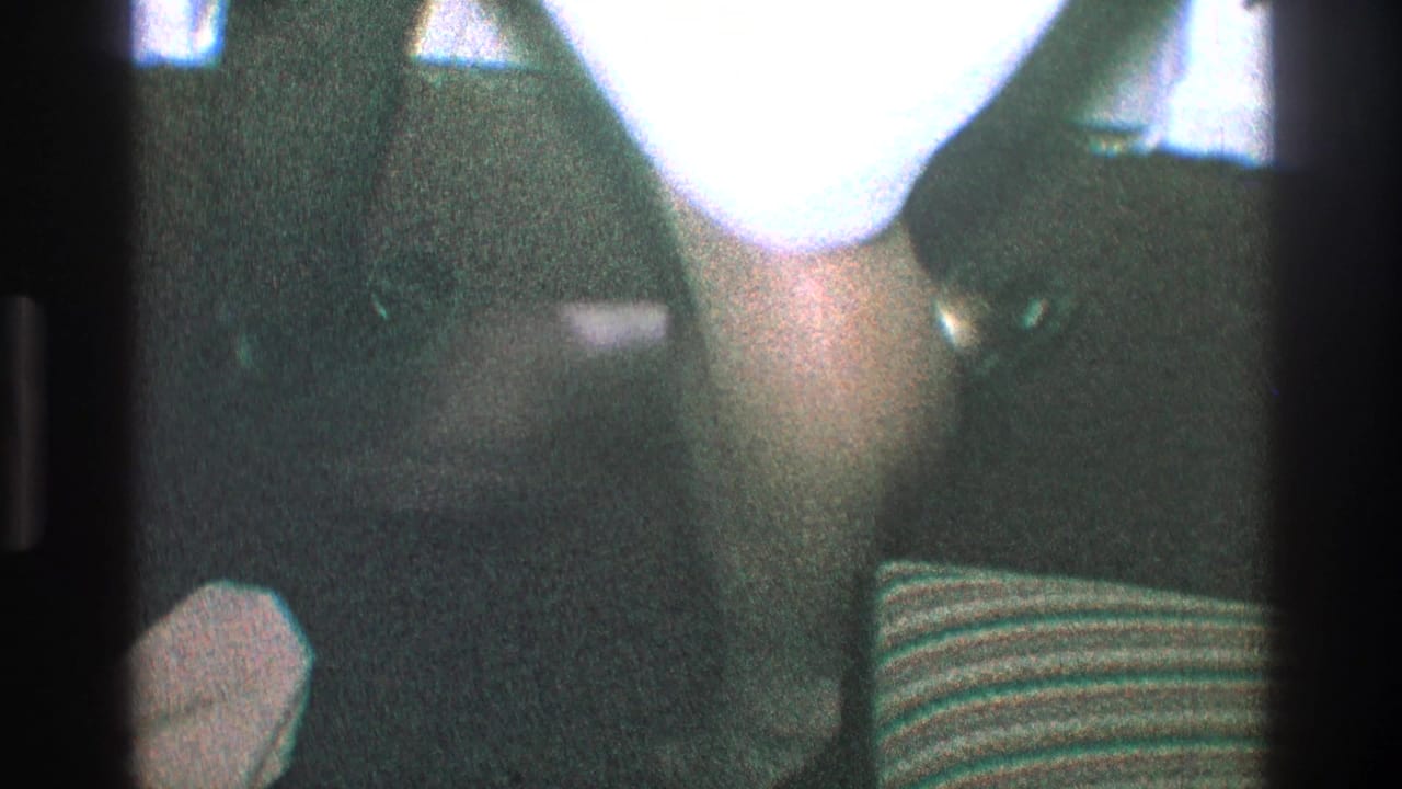 Low indoor view with a bright light area, dark clothing, shoes, and a striped cushion at the side.
