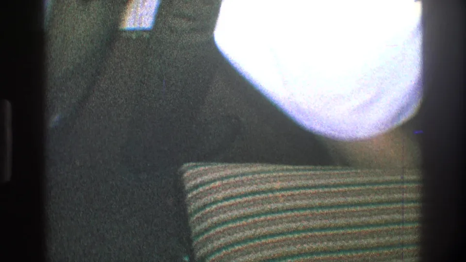 Low 1968 Toledo home-movie frame with a dancer's lower body, bright overexposed shirt area, dark clothing, and striped cushion.