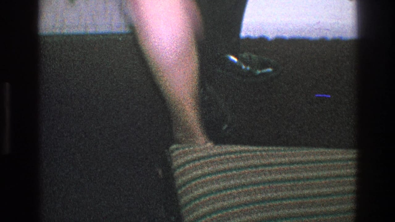 Partial view of dressed adults indoors, with a striped seat or cushion in the foreground.