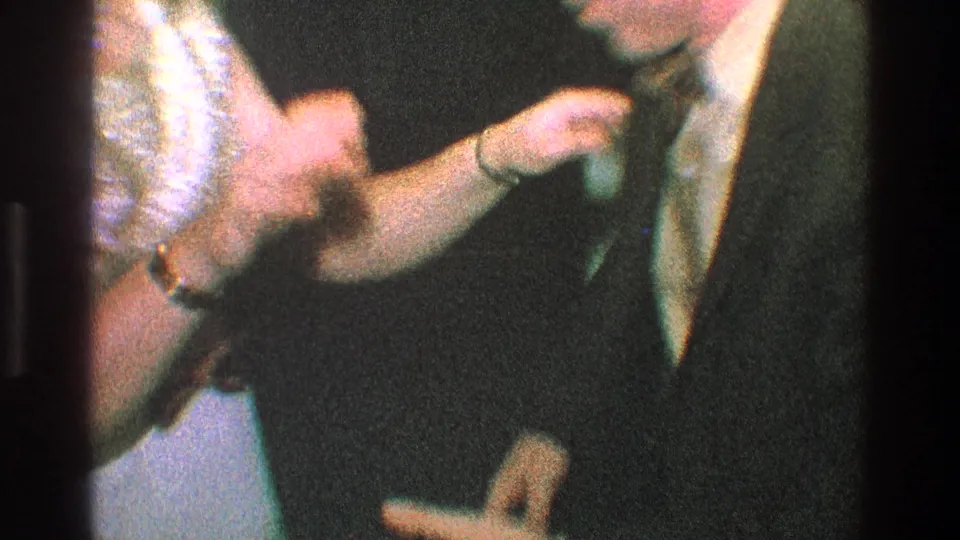 A suited man and a woman in a light dress appear to meet hands during a playful indoor gesture in 1968 Toledo footage.