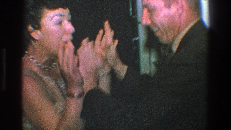 In the clearest 1968 Toledo frame, a woman in a light dress and a suited man face each other with raised hands while laughing or talking.