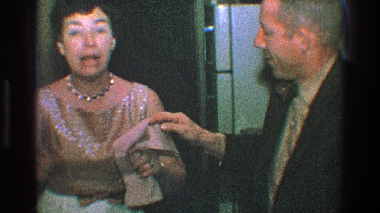 Woman in a gold dress reacts as a suited man reaches toward her arm indoors.