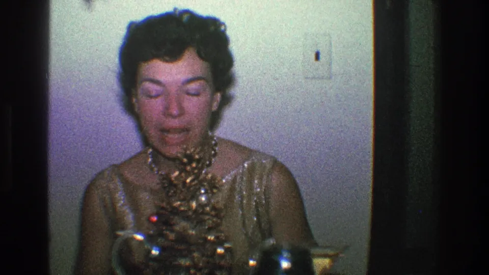 A woman in a gold dress and pearl necklace appears near a table with party items inside a Toledo home in 1968 footage.