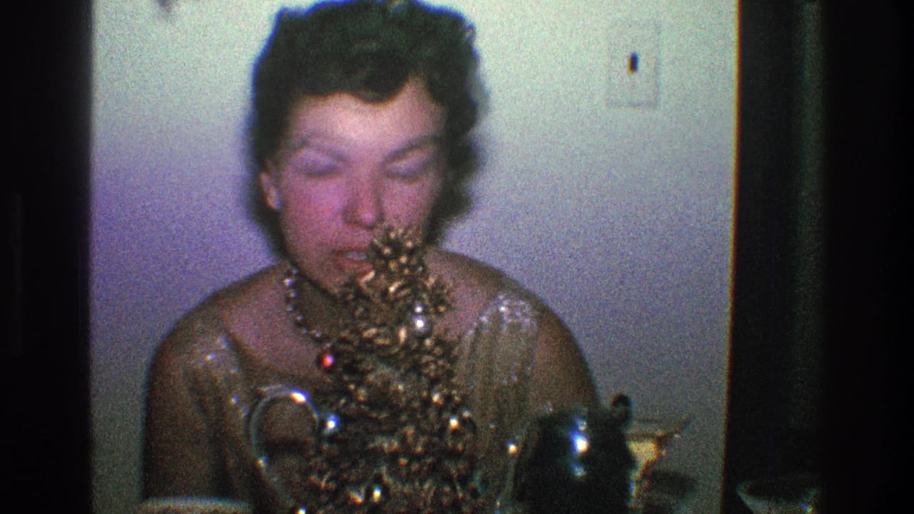 In a 1968 Toledo home-movie frame, a woman in sparkly attire sits at a table behind a small decorated Christmas tree.