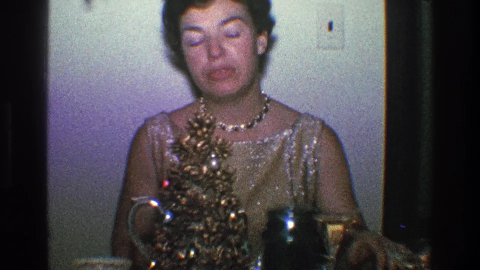A seated woman in formal sparkly attire faces forward behind a small decorated Christmas tree in a Toledo home interior.