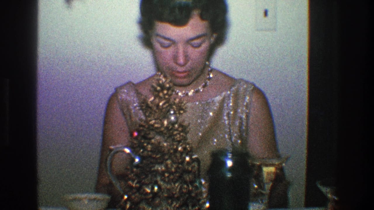 Woman in a gold dress looks down beside a small decorated tree on a table.