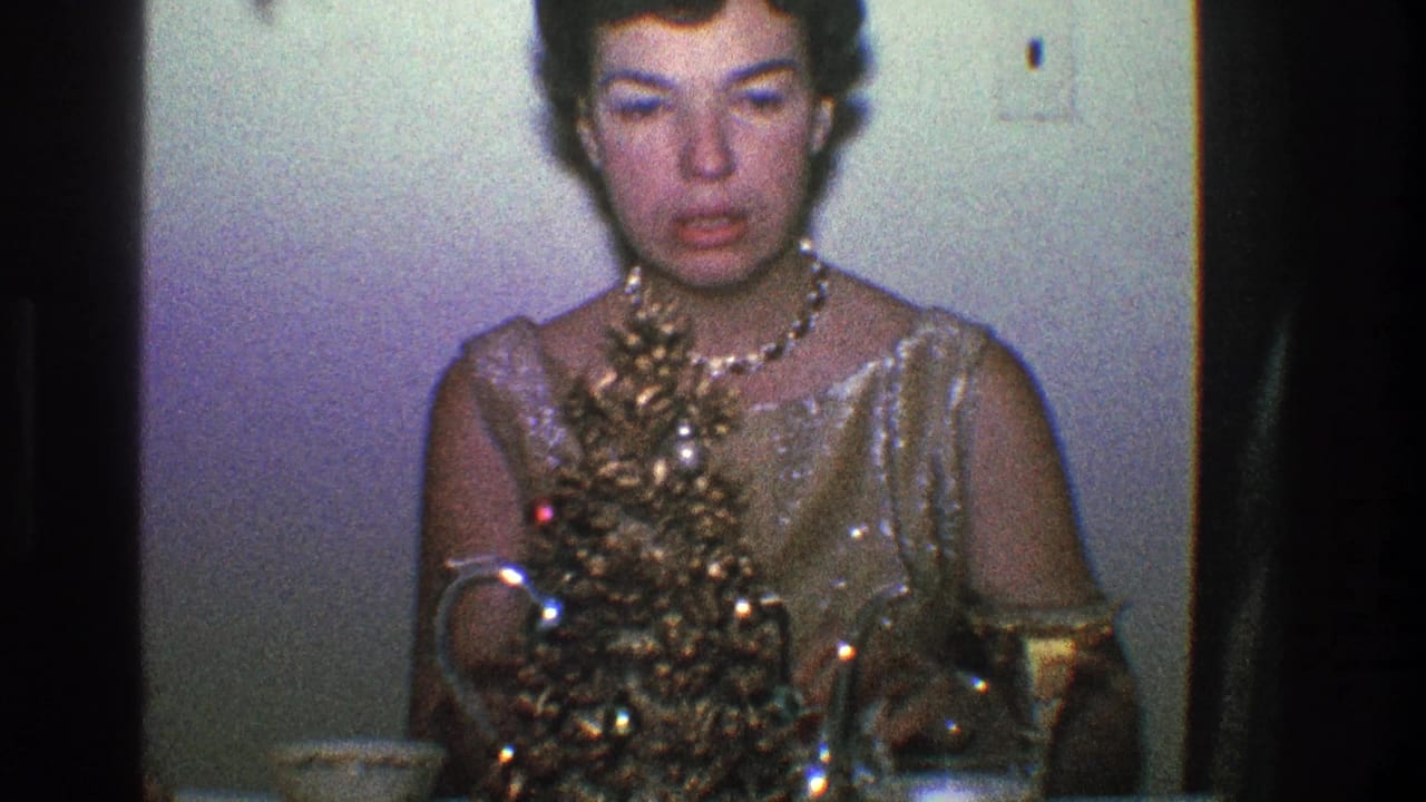 Woman in gold dress faces forward near a decorated table and pale wall.