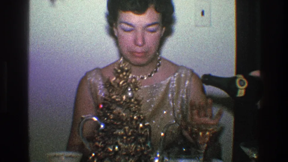 The woman raises a hand toward an offscreen bottle offer, appearing to decline a drink at the 1968 Toledo indoor holiday gathering.