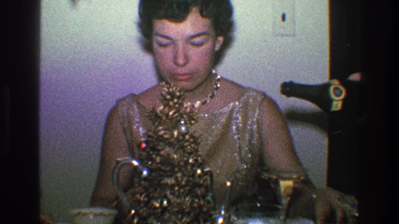 In a 1968 Toledo, Ohio home interior, a woman in a sequined dress and pearl necklace arranges a miniature Christmas tree on a table.