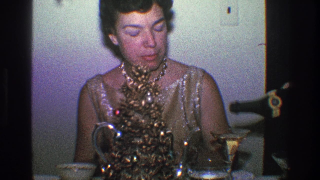 Woman looks down while adjusting a tabletop Christmas tree beside drinks and glassware.