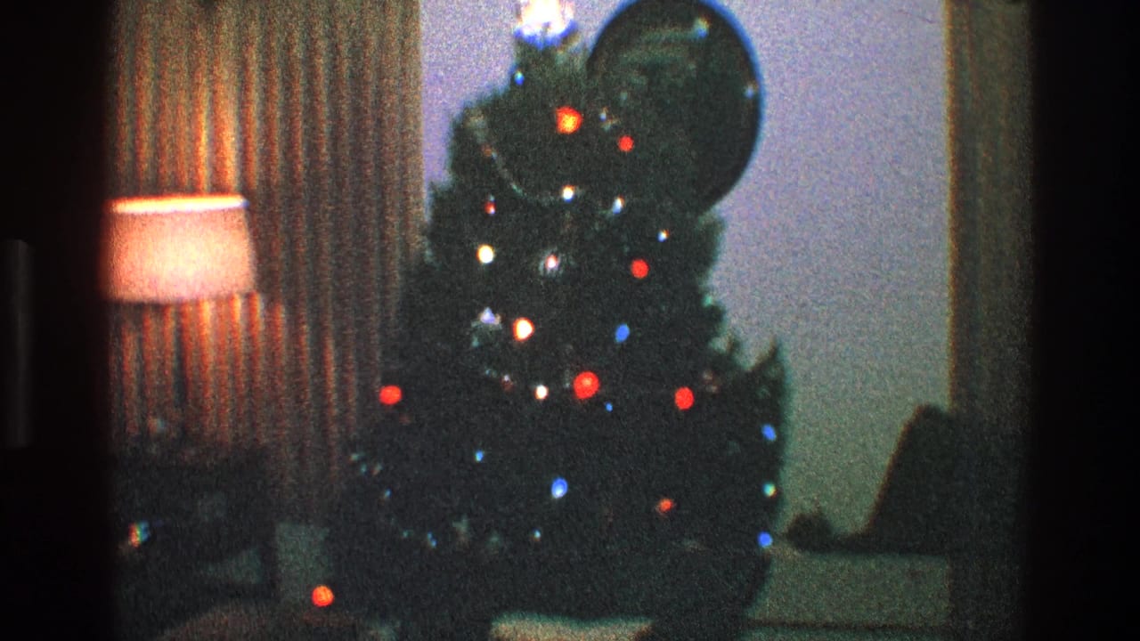 Christmas tree with colored bulbs, lamp, curtains, and window area in a living room.