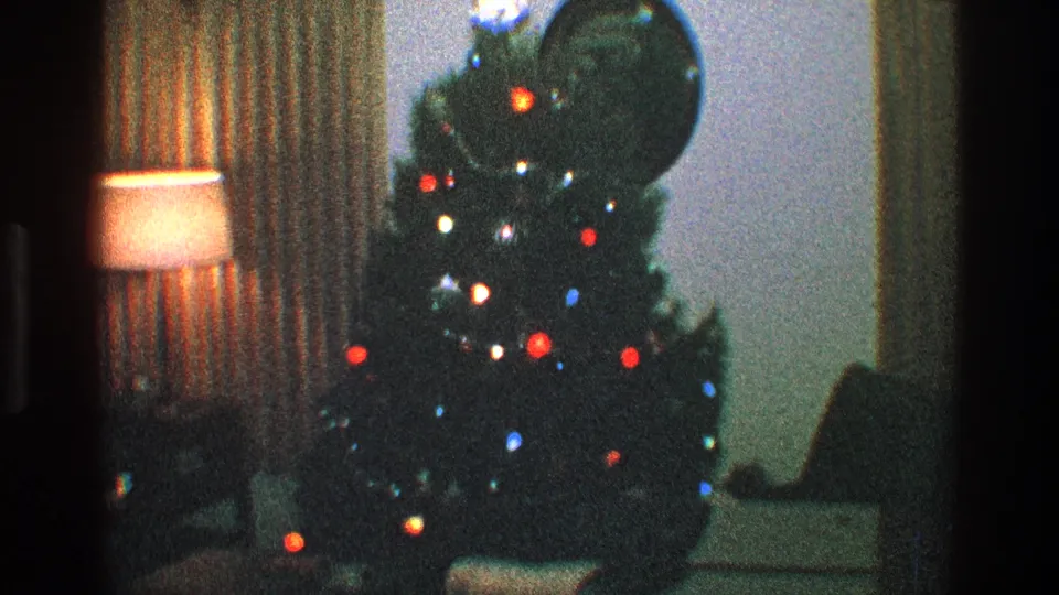 Grainy 1968 Toledo home-movie frame showing a decorated Christmas tree, glowing lamp, and patterned curtains.